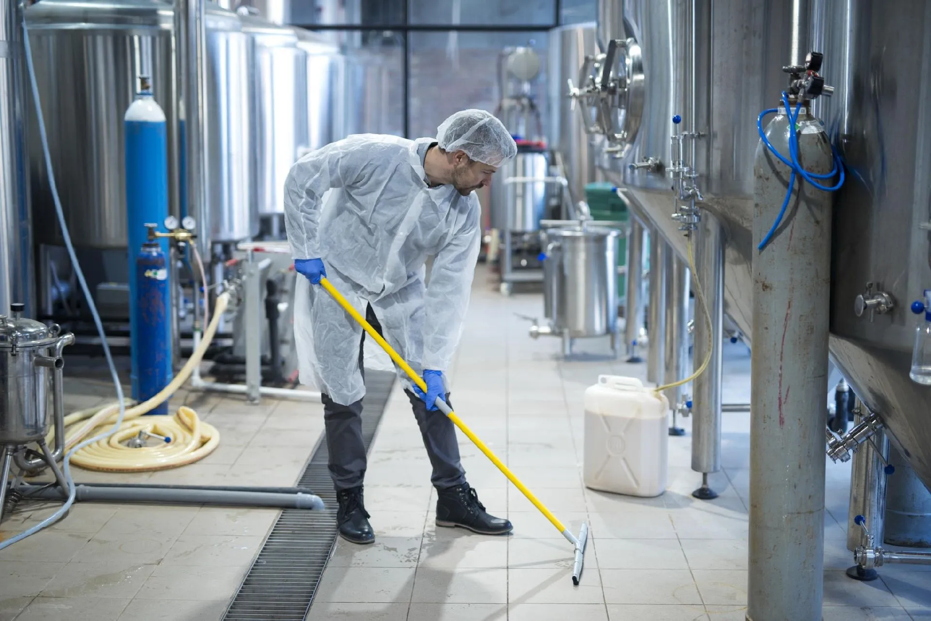 Pulizie professionali in impianto industriale con operatore in tuta protettiva e mop igienizzante